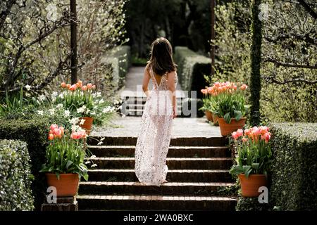 Schöne Passform kurvige junge asiatische Frau transparentes Paillettenkleid stehend in einem Garten Tulpen Pink Stockfoto