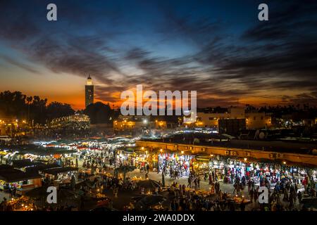 Blick bei Sonnenuntergang auf einen überfüllten Platz Jemaa El Fna, mit der Koutoubia Moschee im Hintergrund, Marrakesch, Marokko Stockfoto