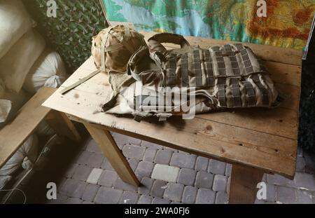 Ein Militärhelm eines ukrainischen Soldaten mit einer schweren kugelsicheren Weste auf einem Holztisch im Innenraum des Kontrollpunktes Stockfoto