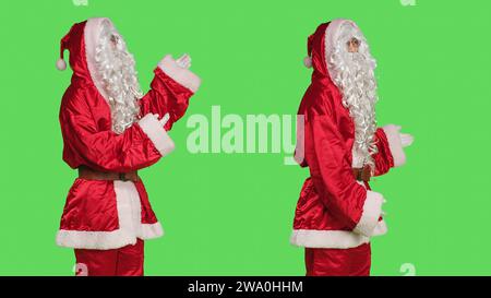 Der weihnachtsvater zeigt etwas, während er mit dem festlichen Kostüm des Stanta claus vor dem Hintergrund des Grünschirms steht. Mann gekleidet wie saint Nick, Weihnachtsmarketing-Kampagne. Stockfoto