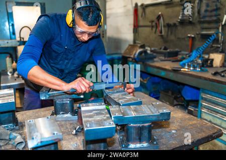 Ein lateinamerikanischer Bediener, der Messungen mit dem Messschieber auf einem Fräser in einer Werkstatt für numerische Steuerung durchführt, High-Tech durch ein CNC-bearbeitungszentrum Stockfoto