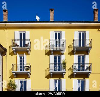 Hellgelbe Fassade mit Fenstern, weißen Fensterläden, Balkonen mit schmiedeeisernen Gittern und Palmen vor einem tiefblauen Himmel in Ascona, Bezirk Lo Stockfoto