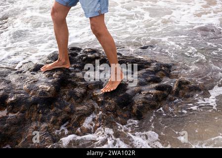 Salvador, Bahia, Brasilien - 29. Januar 2022: Eine Person auf den dunklen und rutschigen Felsen des Rio Vermelho Strandes in Salvador, Bahia. Stockfoto