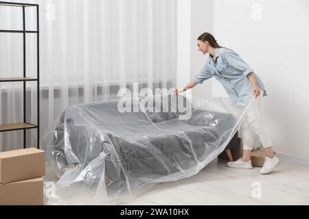 Junge Frau, die Plastikfolie zu Hause vom Sofa weglegt Stockfoto