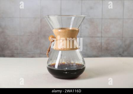 chemex Glaskaffeemaschine mit leckerem Tropfkaffee auf weißem Tisch Stockfoto