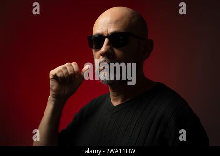 Hübscher, kahlköpfiger und bärtiger Mann in Sonnenbrille, ernsthaft und selbstbewusst posiert zum Foto. Isoliert auf rotem Hintergrund. Stockfoto