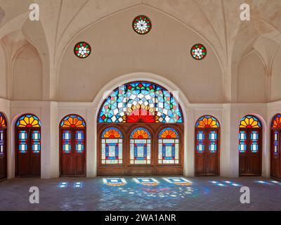 Großer Raum mit bunten Buntglasfenstern im Tabatabaei House, einem historischen Herrenhaus, das um 1880 in Kaschan, Iran, erbaut wurde. Stockfoto