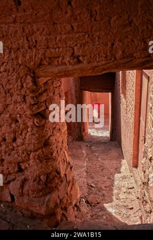 Frau mit rotem Schirm geht durch eine enge Gasse im historischen Dorf Abyaneh, Natanz County, Iran. Stockfoto