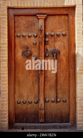 Alte Holztür von Sultan Amir Ahmad Bathhouse mit zwei verschiedenen Klopfern - Metallstab für Männer und Metallring für Frauen. Kaschan, Iran. Stockfoto