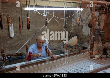 Ein älterer Mann arbeitet an einem horizontalen Webstuhl in der Webwerkstatt. Kaschan, Iran. Stockfoto