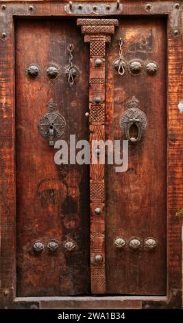 Aufwendig dekorierte massive alte Holztür eines Hauses mit zwei verschiedenen Klopfern - Metallstab für Männer und Metallring für Frauen. Kaschan, Iran. Stockfoto