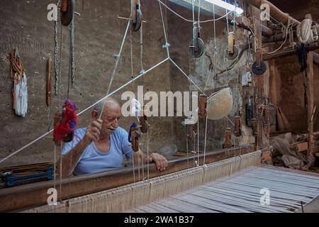 Ein älterer Mann arbeitet an einem horizontalen Webstuhl in der Webwerkstatt. Kaschan, Iran. Stockfoto