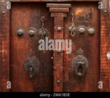 Detail einer alten hölzernen Haustür eines Hauses mit zwei verschiedenen Klopfern - Metallstab für Männer und Metallring für Frauen. Kaschan, Iran. Stockfoto