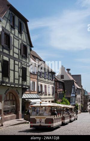 Ein kleiner Touristenzug fährt durch die Straßen des malerischen Dorfes Riquewihr im Elsass, Frankreich. Charakteristisches farbenfrohes traditionelles Halbholz Stockfoto