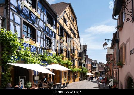 Stadtlandschaft mit traditionellen, farbenfrohen Fachwerkhäusern und Restaurants im sonnigen Riquewihr im Elsass, Frankreich Stockfoto