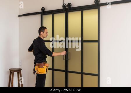 Ein hübscher junger Mann, der doppelte Schiebetür in der Terrasse installiert Eine neue Hausbaustelle Stockfoto