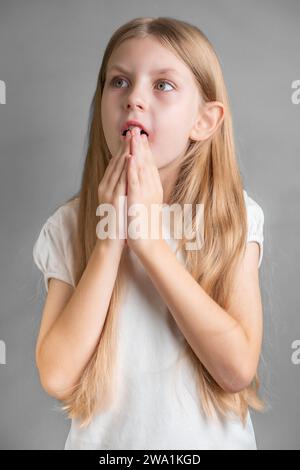 Porträt eines überraschten kleinen Mädchens, eines Mädchens mit langen blonden Haaren in weißem T-Shirt Stockfoto