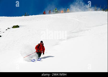 Ein Mann Skifahren im Pulverschnee, während eine Gruppe einen Bergort in der Nähe von South Lake Tahoe, Kalifornien, anschaut. Stockfoto