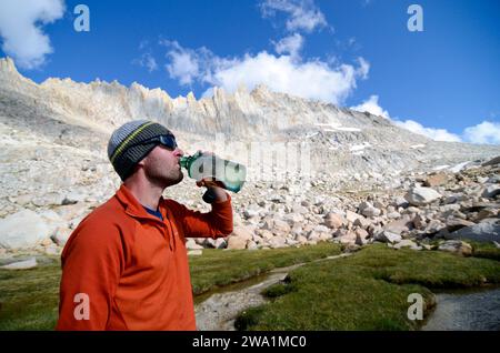Ein Mann trinkt aus seiner Wasserflasche unter dem Feather Peak auf der Sierra High Route, CA. Stockfoto