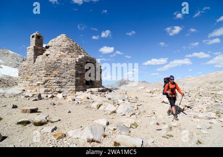 Ein Rucksacktouristen spaziert an der berühmten Muir Hut auf dem Gipfel des Muir Pass auf dem John Muir Trail und der Sierra High Route, CA. Stockfoto