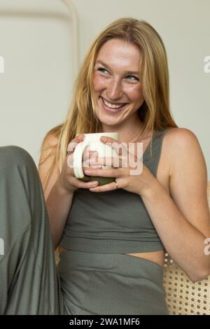 Die lachende junge Frau genießt Morgenkaffee im ruhigen Schlafzimmer Stockfoto