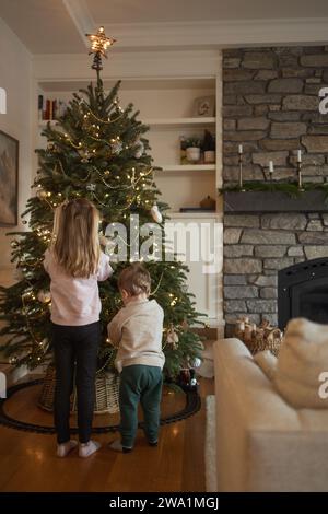 Bruder und Schwester schmücken leise den weihnachtsbaum der Familie Stockfoto