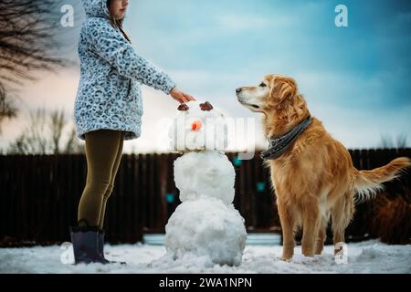 Mädchen baut Schneemann mit ihrem Gold Retriever Stockfoto