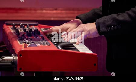 Bild der Hand eines Musikers auf den Tasten eines roten Elektrodenklaviers Stockfoto