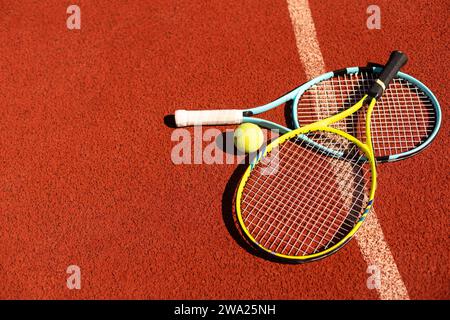 Bälle und Schläger liegen auf einem lehmbraunen professionellen Tennisplatz in der Nähe von Tennisbällen und Schläger auf Schlacke auf dem Tennisplatz auf dem Spielplatz Stockfoto