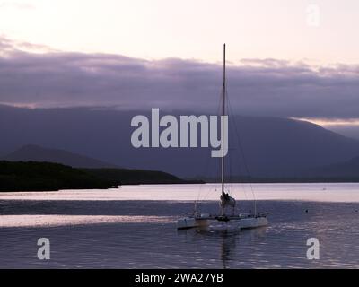 Blick auf den Sonnenuntergang über den fernen Hügeln und einen Katamaran im Vordergrund in Port Douglas Queensland Australien Stockfoto