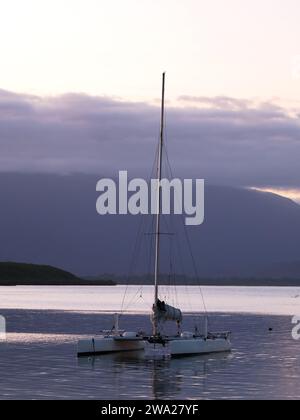 Blick auf den Sonnenuntergang über den fernen Hügeln und einen Katamaran im Vordergrund in Port Douglas Queensland Australien Stockfoto