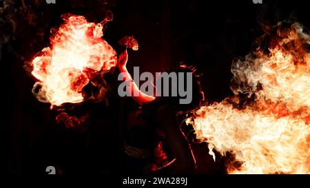 Die Silhouette einer Tänzerin, die glitzernden Schmuck hält und im Dunkeln scharf aussieht, während nachts ein Feuer im Hintergrund brennt Stockfoto