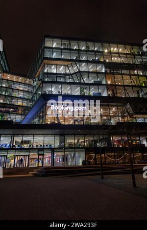 Nächtlicher Blick auf den Hauptsitz von Booking.com in Amsterdam, Niederlande, mit beleuchteten Fenstern in der Glasfassade Stockfoto