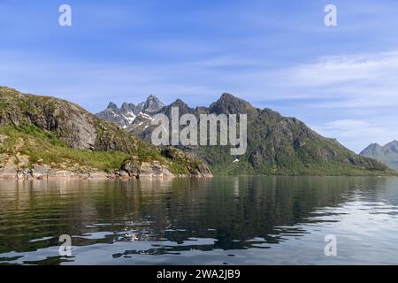 Das spiegelartige Wasser des Trollfjorden spiegelt die Pracht der Lofoten wider, mit schneebedeckten Flecken, die die zerklüfteten grünen Hänge des Berges betonen Stockfoto