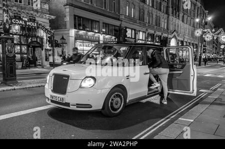 Eine Person steigt nachts in ein weißes Taxi in London, England Stockfoto