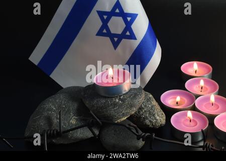 Steine, David-Stern, Kerzen, Stacheldraht, Israel-Flagge auf dunklem Hintergrund. Holocaust-Konzept. Stockfoto