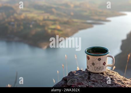 Emaille-Kaffeetasse auf dem Felsen am Aussichtspunkt mit Blick auf den See mit Kopierraum für Text. Selektiver Fokus. Stockfoto