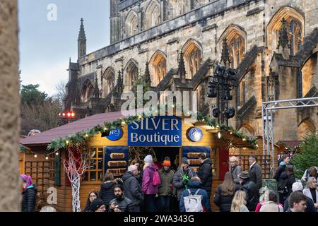 Besucher des Weihnachtsmarktes in Winchester Cathedral shoppen und in handwerklich hergestellten Hütten mit Winchester Cathedral im Hintergrund stöbern. England Stockfoto