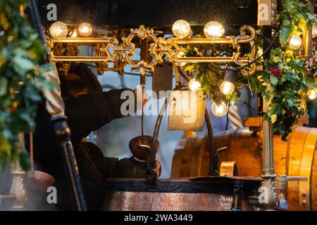 Eine Frau, die Gluhwein (Glühwein) aus einem heißen Kupferkessel auf dem Winchester Cathedral Christmas Market in Hampshire, Großbritannien, in eine Tasse hüllt Stockfoto