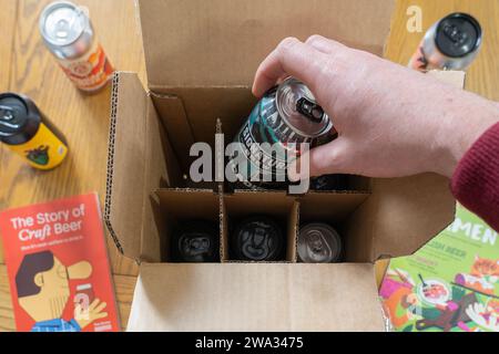 Eine Hand, die ein Craft-Bier aus einer Lieferbox zu Hause nimmt – Beer52 ist ein britischer Craft-Beer-Abonnementclub. Thema: Zu Hause trinken, Craft-Biere Stockfoto