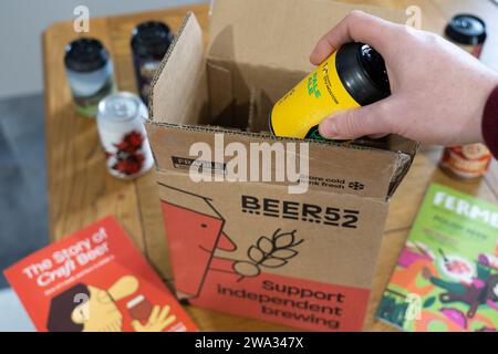 Eine Hand, die ein Craft-Bier aus einer Lieferbox zu Hause nimmt – Beer52 ist ein britischer Craft-Beer-Abonnementclub. Thema: Zu Hause trinken, Craft-Biere Stockfoto