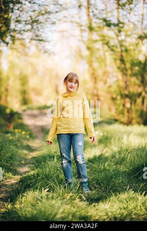 Außenporträt eines hübschen kleinen Mädchens im Frühlingswald mit grüner Bluse und Jeans Stockfoto