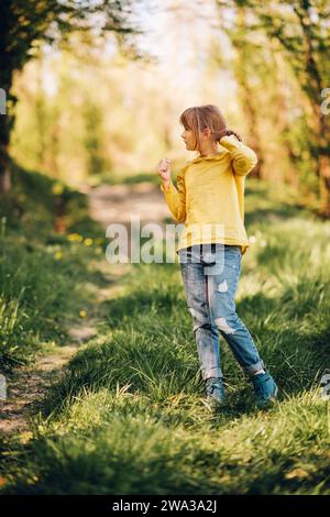 Außenporträt eines hübschen kleinen Mädchens im Frühlingswald mit grüner Bluse und Jeans Stockfoto