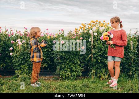 Zwei lustige Kinder spielen zusammen im wunderschönen Chrysanthemen-Garten. Kleiner hübscher Junge mit Kamera, der Fotos von seiner süßen Schwester macht. Familienzeit in Stockfoto
