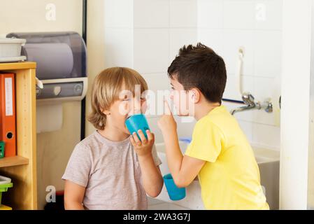 Zwei Kinder im Klassenzimmer, Jungs trinken Wasser in der Schule, halten Plastikgläser Stockfoto