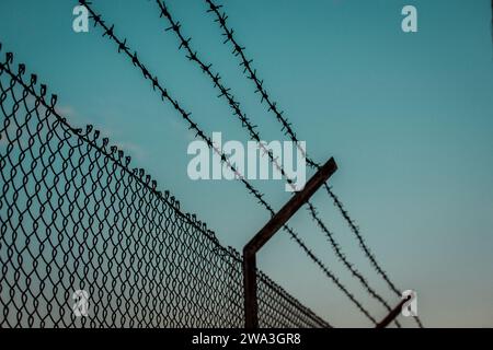 Stacheldraht gegen blauen Himmel. Industriezone geschützt durch einen Gitterzaun. Lager, Fabrikgebiet. Privatgrundstück. Gefängnis, Gefängniszone. Stockfoto