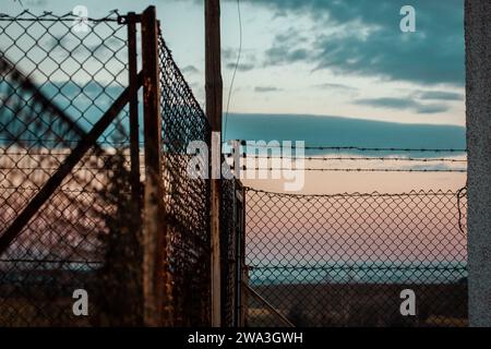 Stacheldraht gegen blauen Himmel. Industriezone geschützt durch einen Gitterzaun. Lager, Fabrikgebiet. Privatgrundstück. Gefängnis, Gefängniszone. Stockfoto