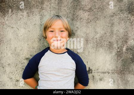 Outdoormodeporträt des entzückenden 5-6-jährigen kleinen blonden Jungen, der ein T-Shirt trägt Stockfoto