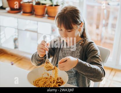 Kleines Mädchen isst Spaghetti Bolognese zu Hause zum Mittagessen Stockfoto