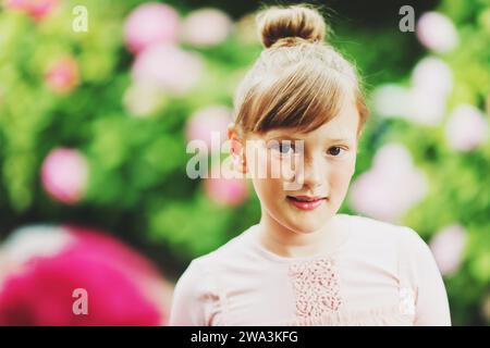 Außenporträt eines hübschen kleinen Mädchens, das mit wunderschönen Hortensie-Blumen im Sommergarten spielt, ein Kleid im Ballerina-Stil trägt, Haarkochen Stockfoto